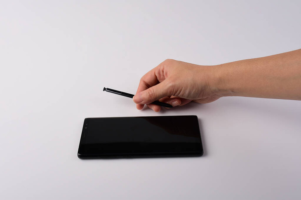Kéz- és okostelefon és fekete stylus írás elszigetelt fehér háttér.  - Fotó, kép