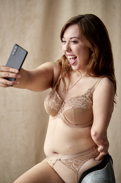 Studio Shot Of Body Positive Woman With Prosthetic Limb In Underwear Taking Selfie On Mobile Phone - Fotografie, Obrázek