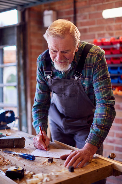 Senior Male Carpenter In Garage Workshop Sketching Out Design On Paper - Foto, afbeelding