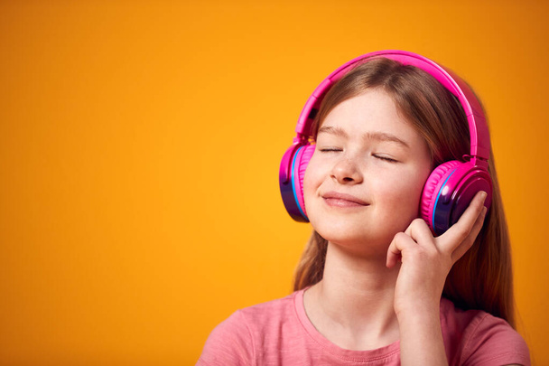Studio Shot Of Smiling Young Girl Listening To Music On Headphones Against Yellow Background - Zdjęcie, obraz