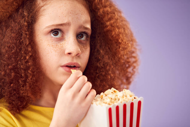 Scared Girl Watching Horror Movie And Eating Popcorn At Cinema Against Purple Background - Photo, image