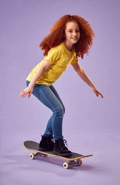 Studio Shot Of Young Girl Riding Skateboard Against Purple Background - Фото, изображение