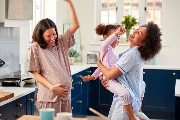 Embarazada familia con dos madres usando pijama bailando en cocina con hija - Foto, imagen