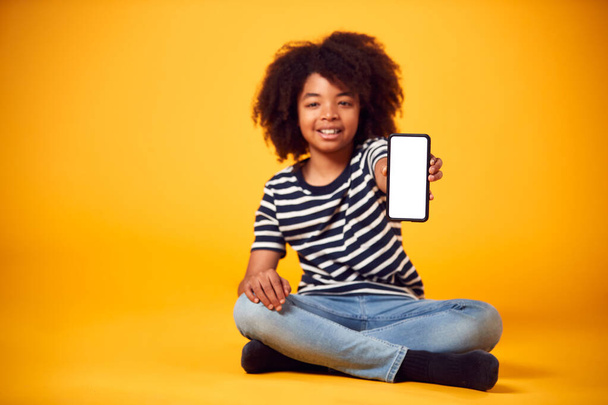 Studio Portrait Of Boy Showing Mobile Phone With Social Media Screen Against Yellow Background - Foto, imagen