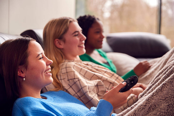 Group Of Multi-Cultural Teenage Girl Friends Snuggled Under Blanket Watching TV At Home - Foto, afbeelding