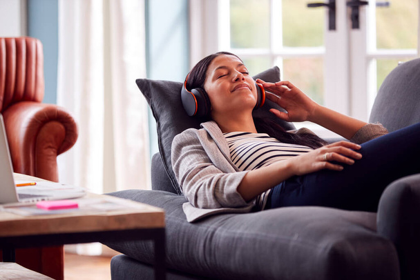 Woman Working From Home Taking A Break Lying On Sofa Listening To Music On Wireless Headphones - Foto, imagen