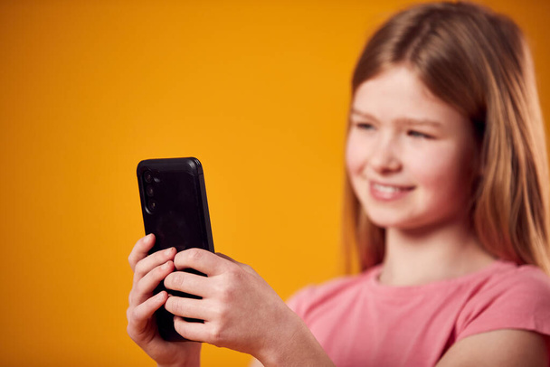 Studio Portrait Of Young Girl Using Mobile Phone Against Yellow Background - Foto, immagini