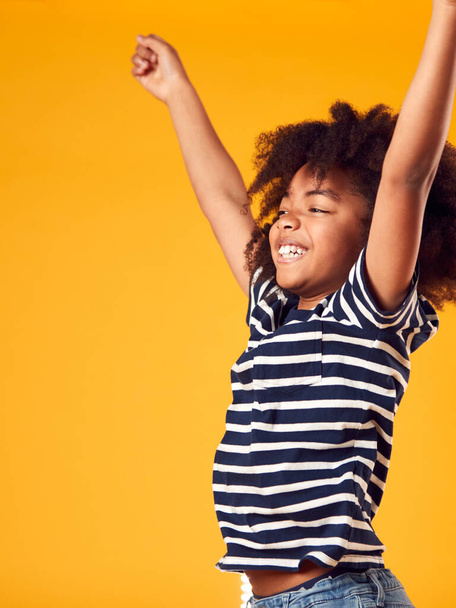 Studio Shot Of Energetic Boy Jumping In The Air With Outstretched Arms Against Yellow Background - Фото, изображение