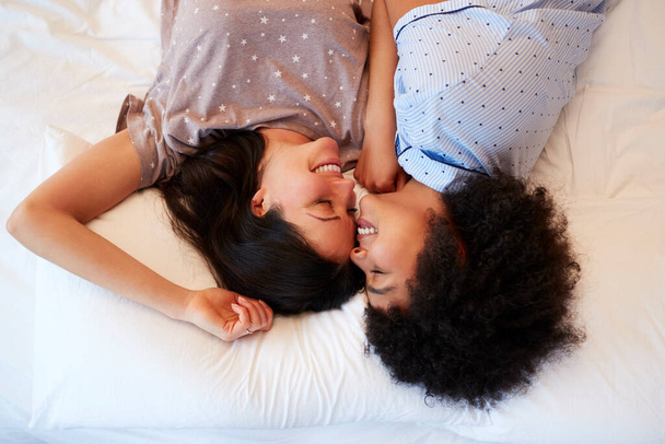 Overhead portret van het houden van hetzelfde geslacht vrouwelijk paar dragen pyjama 's liggend op bed thuis - Foto, afbeelding