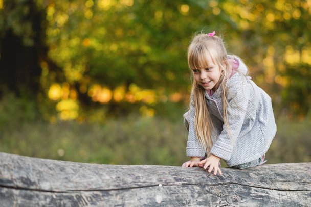 Cute baby girl on all fours balances on a fallen log. - Foto, Imagem