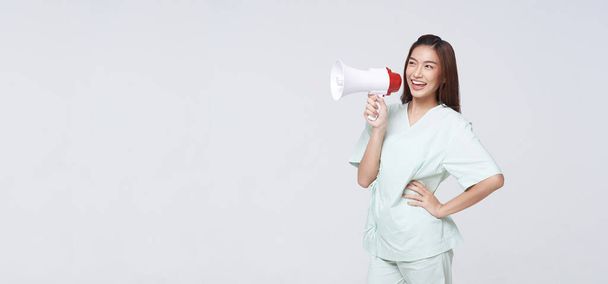 Азиатская пациентка в больничном халате громко кричит, держа в руках мегафон, говорящий о компенсационном покрытии, или говорит страховому агенту или больнице о чрезвычайной ситуации. - Фото, изображение