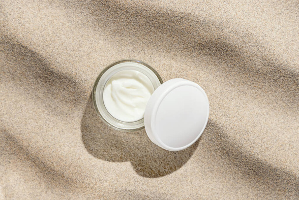 Opened cream jar with white lid on beige sand top view, hard light. Package mockup. Natural skincare product. Facial cosmetics for beauty routine. Zen style, minimal aesthetic - Photo, image