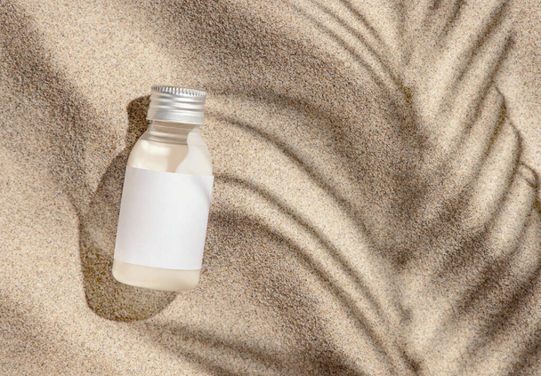 Kozmetikai krém palack üres címkével a bézs homok tetején. Csomagoló mockup. Természetes bőr termék szépség rutin. Nyári napsütéses nap pálmalevél kemény árnyék, trópusi nyaralás hangulat - Fotó, kép