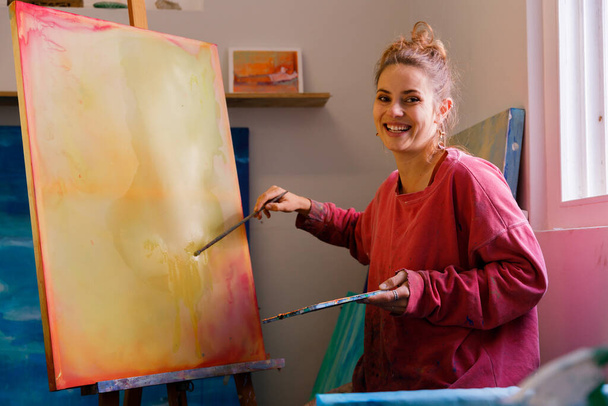 Portrait of Female Artist Works on Abstract Ölgemälde, Moving Paint Pinsel energetisch schafft sie moderne Meisterwerk. Licht-Kreativ-Studio, wo große Leinwand auf Staffelei beleuchtet steht. - Foto, Bild