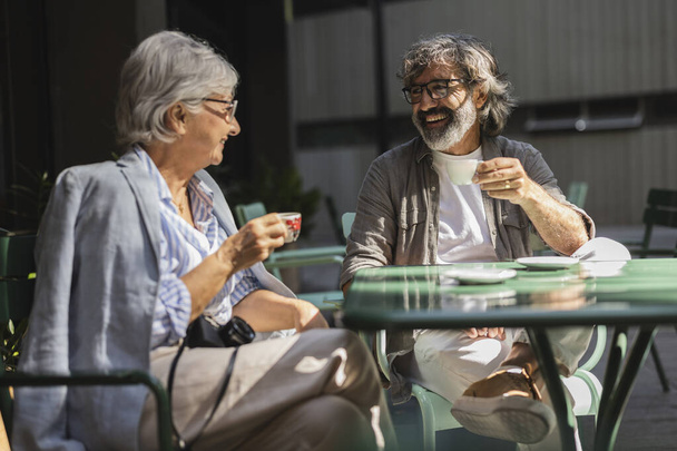 Vidám, mosolygós, fehér idős pár, akik a szabadtéri dohányzóasztalnál pihennek. Romantikus, idős férfi és nő portréja kávézás az étterem teraszán - Fotó, kép