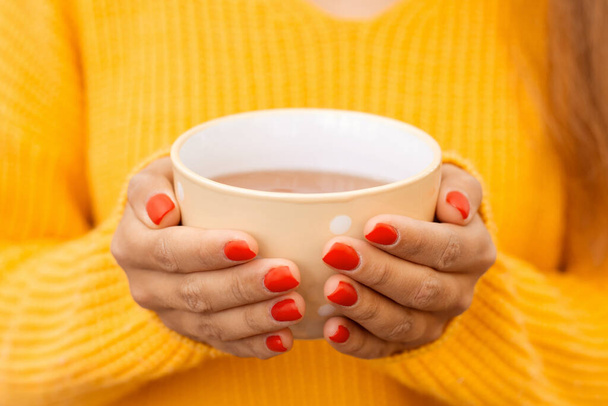 Közelkép egy lányról egy csésze meleg és ízletes teával. Meleg és hangulatos légkör, élénk őszi színek - Fotó, kép