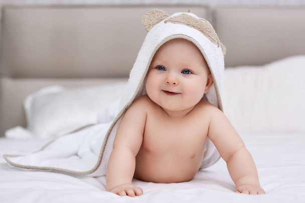 adorable baby girl lies on white bed with towel on her head and body after bath. Hygiene and baby care concept. - Foto, Imagen