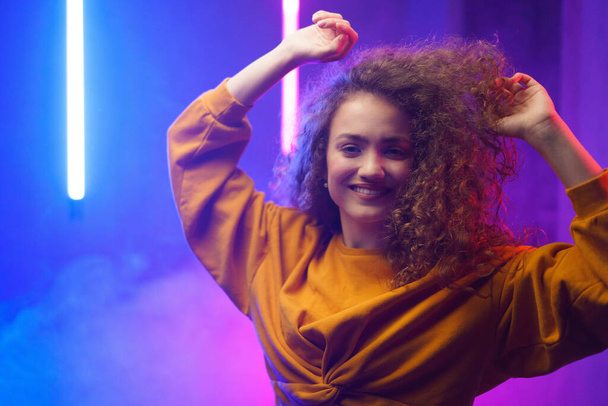 A portrait of a happy young woman dancing over neon light background at disco party - Photo, Image