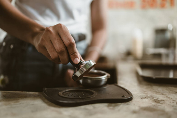 Barista using a tamper to press ground coffee into a portafilter. Coffee maker concept - Zdjęcie, obraz
