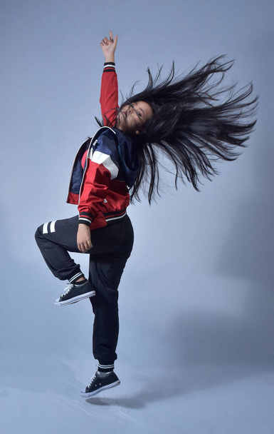 beautiful young Asian female dancer with a long hair flip photo. Full-length body size view of an attractive dreamy cheerful lady posing wind blowing isolated over a bright blue color background - 写真・画像