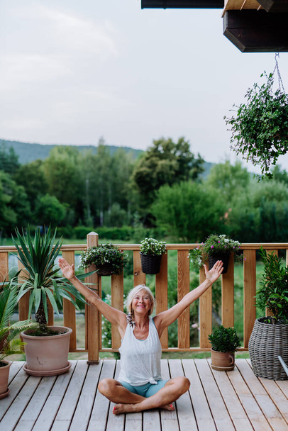 Senior woman sitting outdoors on a terrace in summer, doing yoga exercise. - Foto, immagini