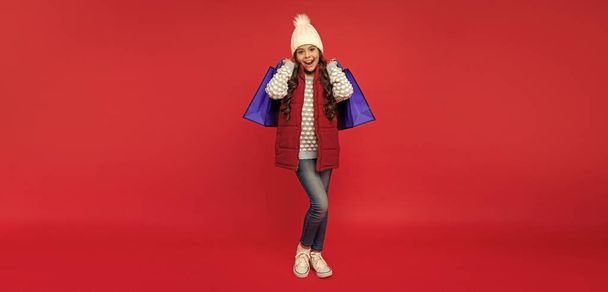 amazed teen girl in with shopping bag. present and gifts buy. shopping child with purchase. kid in hat. happy birthday holiday. black friday discount. seasonal christmas sales. - Foto, afbeelding