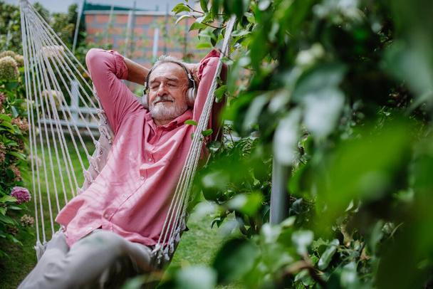 Happy senior man listening music and relaxing in outdoor swing,in a garden. - Fotografie, Obrázek