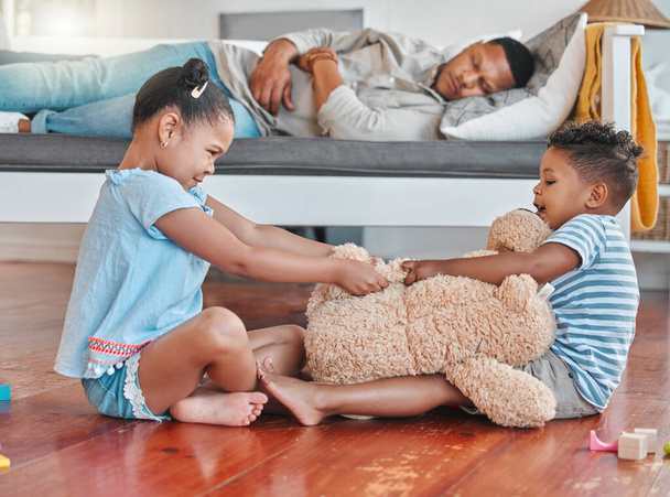 Поки ти спав. два брати і сестри борються за тедді на підлозі, а їх батько спить на дивані вдома
 - Фото, зображення