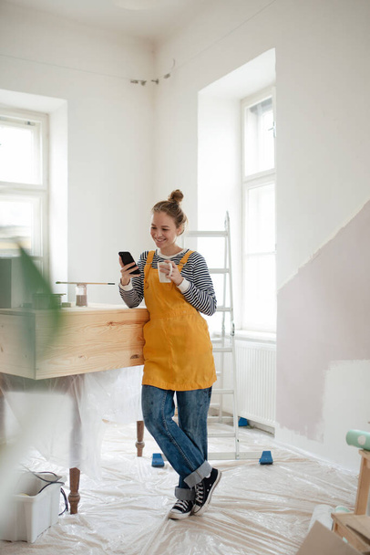 Happy young woman having break during renovation her house. Using phone, searching inspiration at social medias. - Foto, immagini