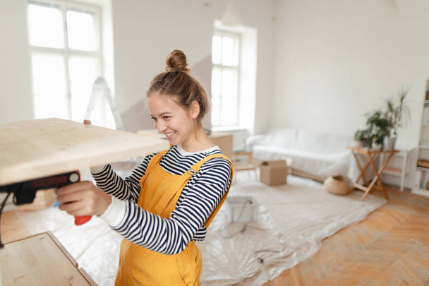 Happy young woman installing wooden shelf in her house. Concept of reusing materials and sustainable lifestyle. - Φωτογραφία, εικόνα