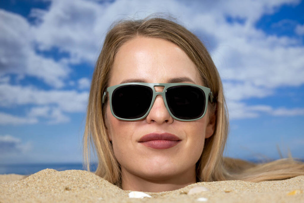 Eine hübsche Frau mit Sonnenbrille bis zum Kopf begraben - Foto, Bild