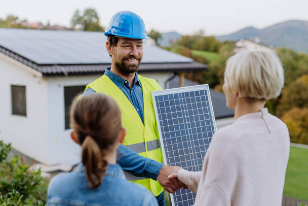 Smiling handyman, photovoltaics panels installer shaking hand with family owner of the house. - Photo, image