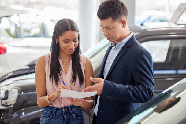 All I need is your signature and the car is yours. a young woman signing paperwork at a car dealership - Photo, Image