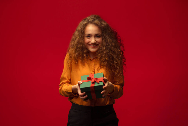 Portrait of happy young woman holding a gift box, red background. - Fotoğraf, Görsel