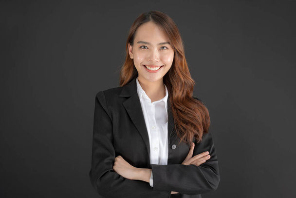 Mujer de negocios vistiendo un traje negro de pie con los brazos cruzados y sonriendo sobre un fondo negro. - Foto, Imagen