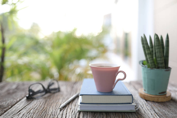 ピンクのコーヒーカップとノートブック、屋外バルコニーで木製のテーブルのSansieveria boncellensisリラックスした作業シーン - 写真・画像