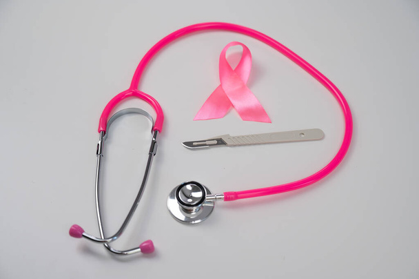 Pink stethophonendoscope, satin ribbon and scalpel on white background - Photo, image