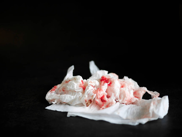 Свежая красная кровь, окрашенная на бумаге, изолированная на темном фоне, использованная смятая салфетка, кровотечение, копировальное пространство - Фото, изображение