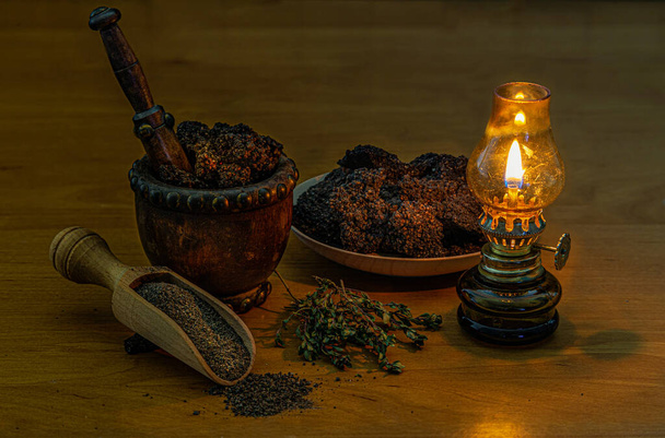 Pieces of black salt by the light of an oil lamp. Food decoration design. Still life of large pieces of salt, grinding in a wooden mortar and laid out on a scoop. Small oil lamp - Photo, Image