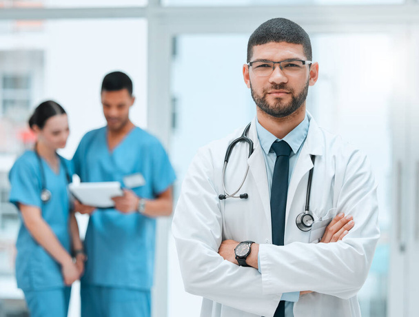 Healthcare is the name of my game. a young male doctor standing with his arms crossed at a hospital - Foto, Imagen