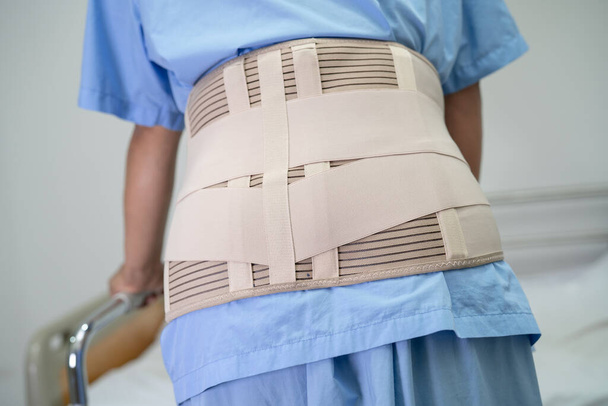 Aasialainen nainen potilas yllään selkäkipu tukivyö ortopedinen lannerangan kanssa kävelijä. - Valokuva, kuva