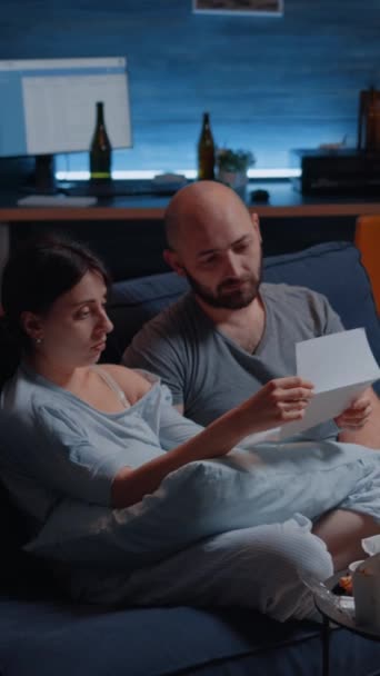 Vídeo vertical: Chocado, preocupado frustrado, confuso, desesperado jovem casal lendo aviso de despejo na carta de papelada sentindo-se impotente. Inquilinos infelizes recusando notificação de aviso para não pagos - Filmagem, Vídeo