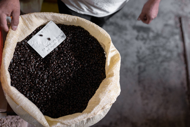 新鮮な濃い焙煎コーヒーでいっぱいの袋を持っている大人の男。地元のコーヒー生産の概念 - 写真・画像