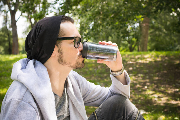 Πλευρική άποψη του ανθρώπου πίνοντας καφέ από επαναχρησιμοποιήσιμο κύπελλο, ενώ περνούν την ημέρα στη φύση.  - Φωτογραφία, εικόνα