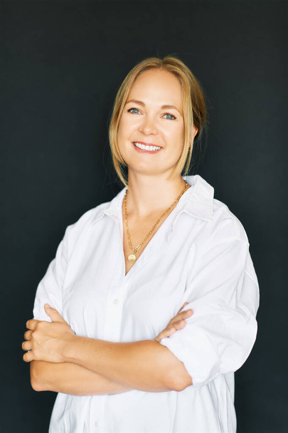 Studio portrait of beautiful confident woman posing on black background, wearing white shirt - Foto, afbeelding
