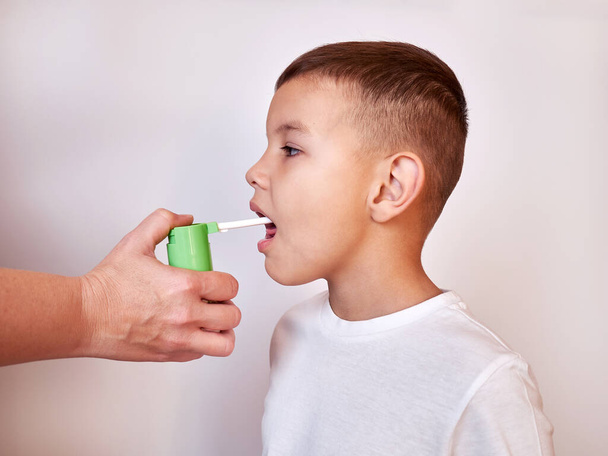 Medicine is sprayed into a sore throat of a little boy. Throat treatment. - Foto, Bild