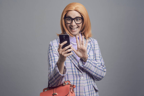 Cheerful woman having a video call with her smartphone, she is waving at the phone screen - Foto, Bild