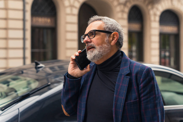 Yakışıklı ve kendine güveni tam, sakallı, beyaz saçlı, olgun bir iş adamı işe giderken telefonda konuşuyor. Yüksek kalite fotoğraf - Fotoğraf, Görsel