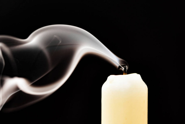 El humo gris de una vela apagada se desarrolla sobre un fondo negro. - Foto, imagen