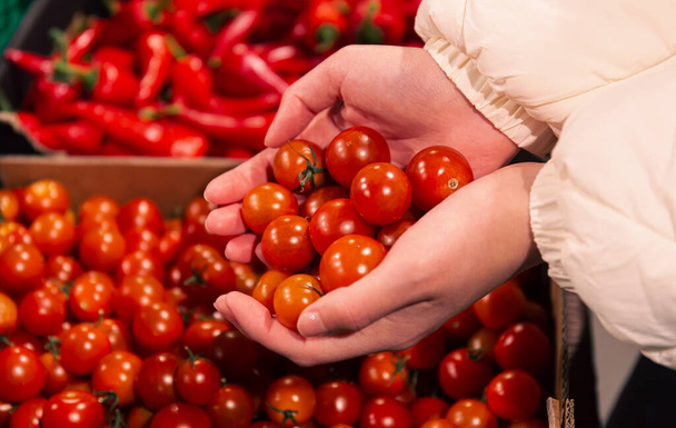 Жінка вибирає вишневі помідори в продуктовому магазині, крупним планом, купуючи органічну їжу для приготування їжі
. - Фото, зображення